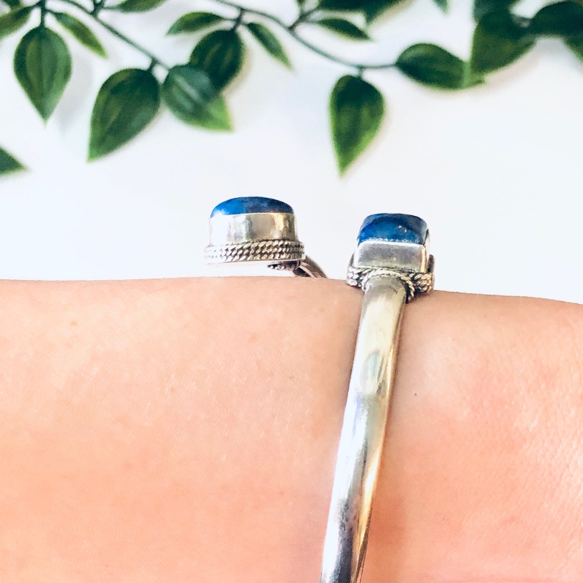 Vintage silver bangle bracelet with blue lapis lazuli stones, worn on wrist with green foliage in background