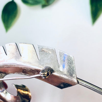 Vintage silver feather brooch pin with abstract curved design, photographed against a white background with green leaves.