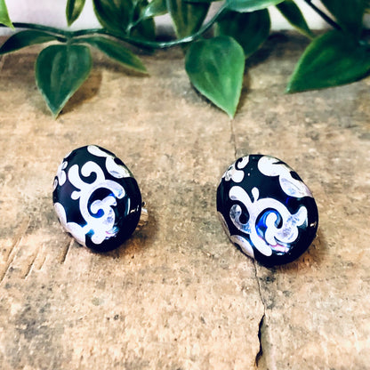 Vintage silver and black swirl design stud earrings on rustic wooden surface with green plant leaves in background