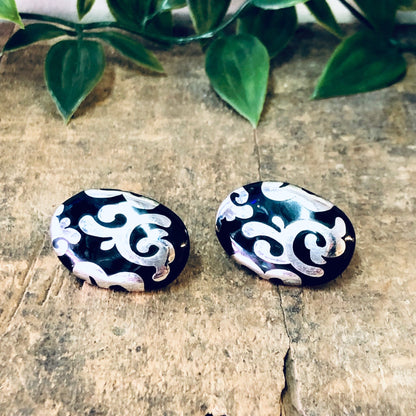 Vintage black and silver swirl design pierced stud earrings on wooden surface with green leaves