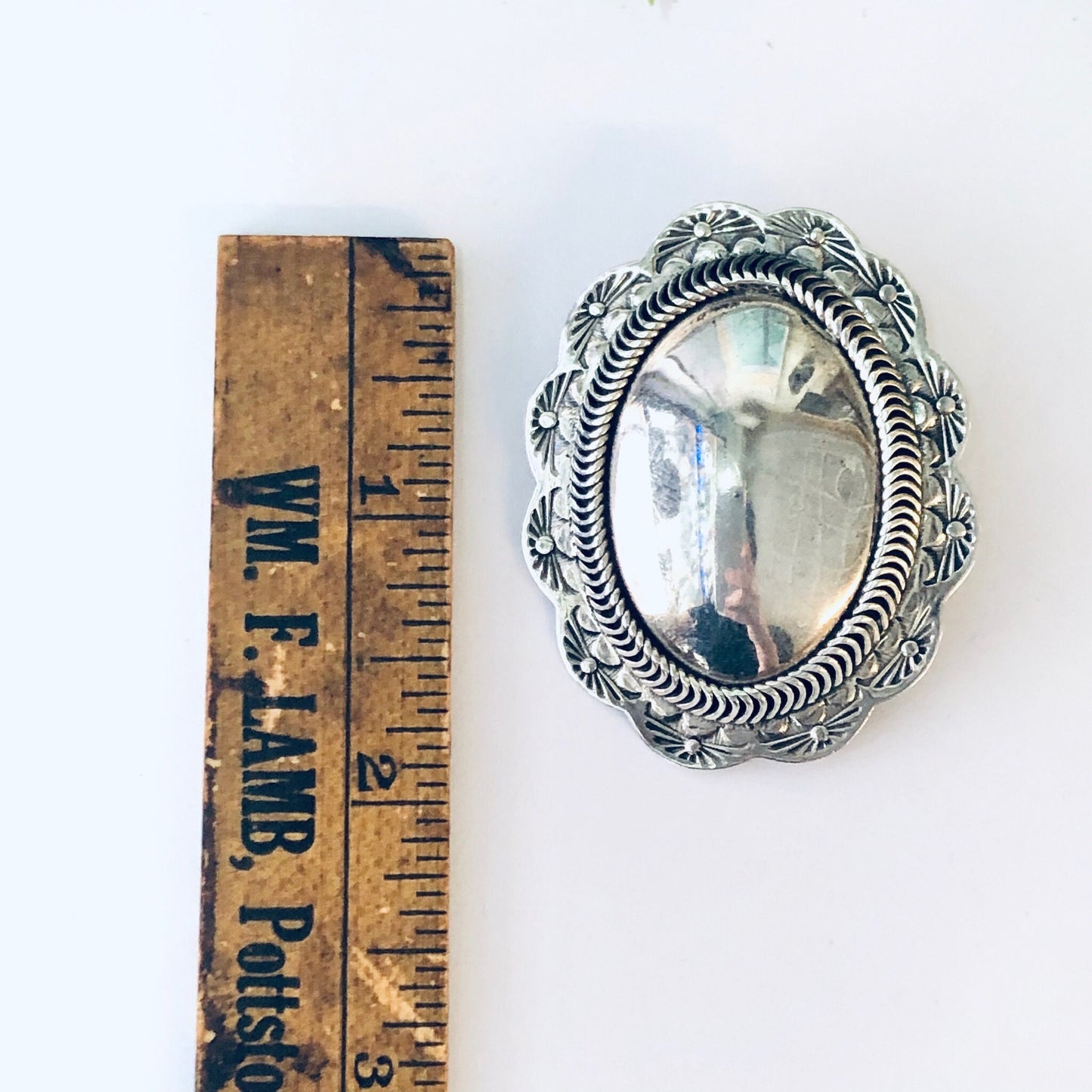 Vintage silver concho clip-on earrings with intricate floral design, shown next to an old wooden ruler for scale. Unique statement jewelry handcrafted in Taxco, Mexico from 925 sterling silver.