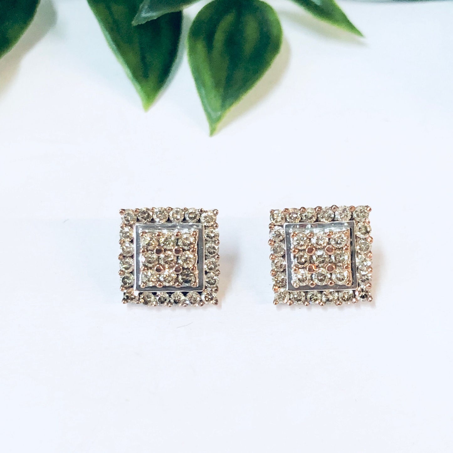 Vintage 10K gold diamond cluster earrings in Art Deco style square stud design, pictured with green leaves on white background.