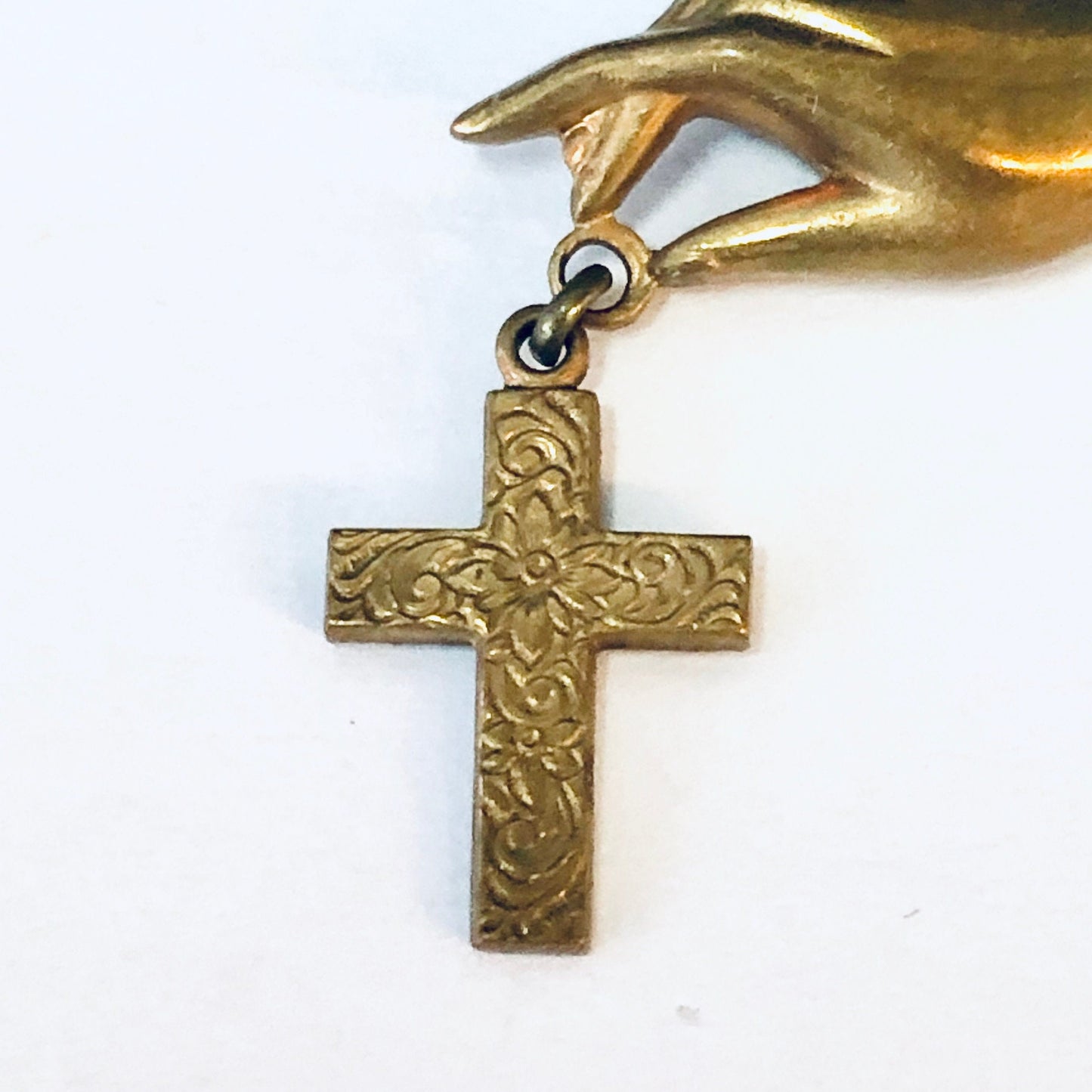 Vintage gold-toned religious cross brooch featuring an ornate design held by a sculpted hand, detailed view of the antique costume jewelry pin against a white background.