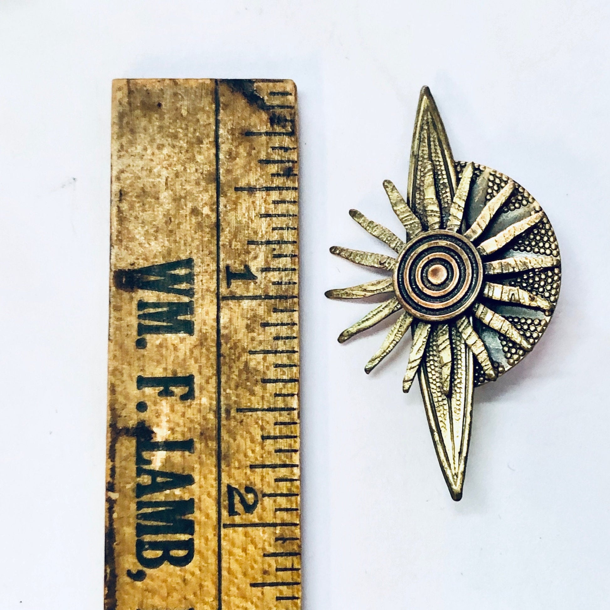 Vintage brass-toned sun-shaped brooch pin next to measuring ruler, depicting radial design resembling solar flares or rays, costume jewelry gift idea