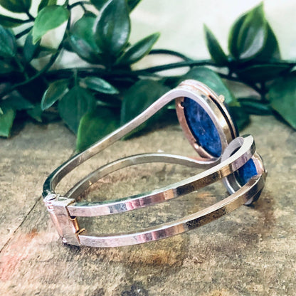 Vintage silver-toned hinged cuff bracelet with blue stone accents on wooden surface with greenery in background