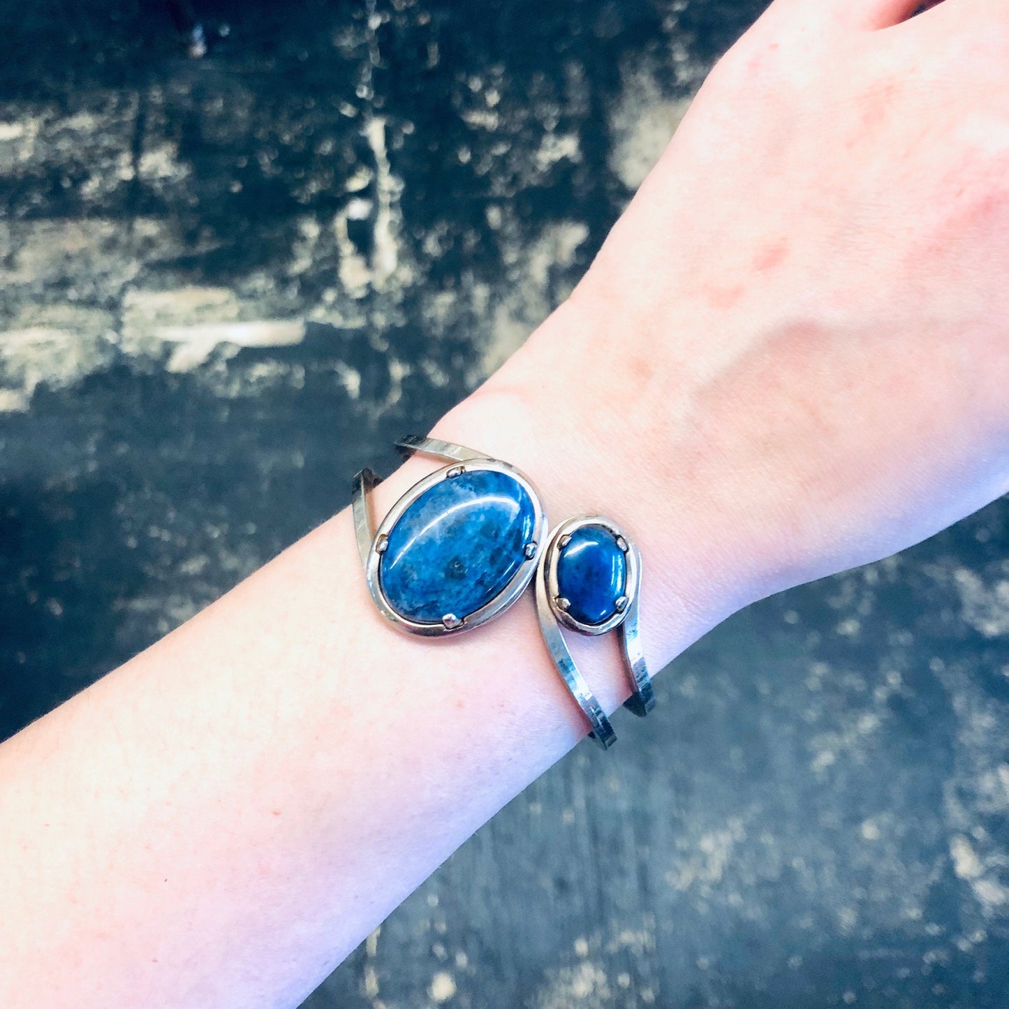 Vintage silver-toned cuff bracelet with oval blue stones on wrist against weathered concrete background