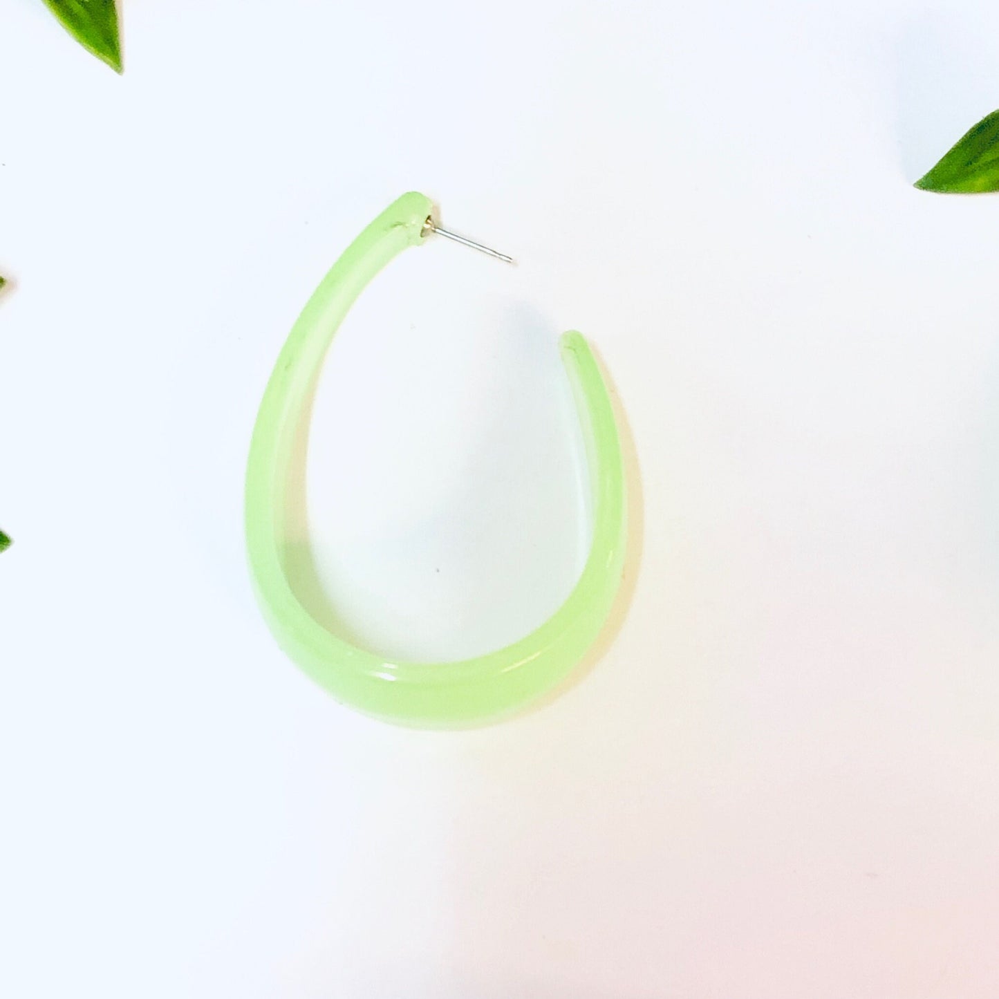 Neon green translucent hoop earrings on white background with leaves