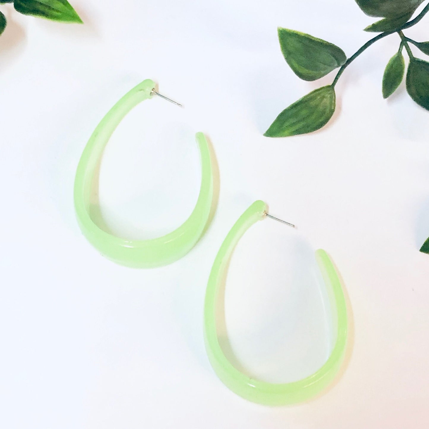 Neon green vintage acrylic hoop earrings from the 1980s on white background with green leaves