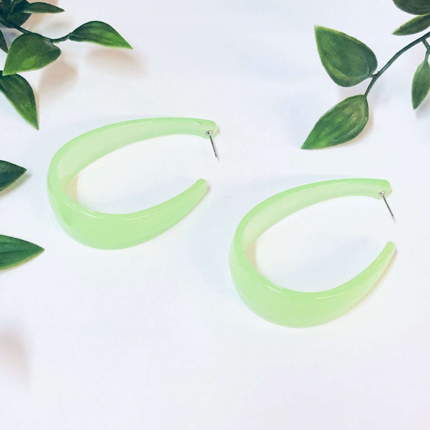 Neon green translucent plastic hoop earrings on white background with green leaves