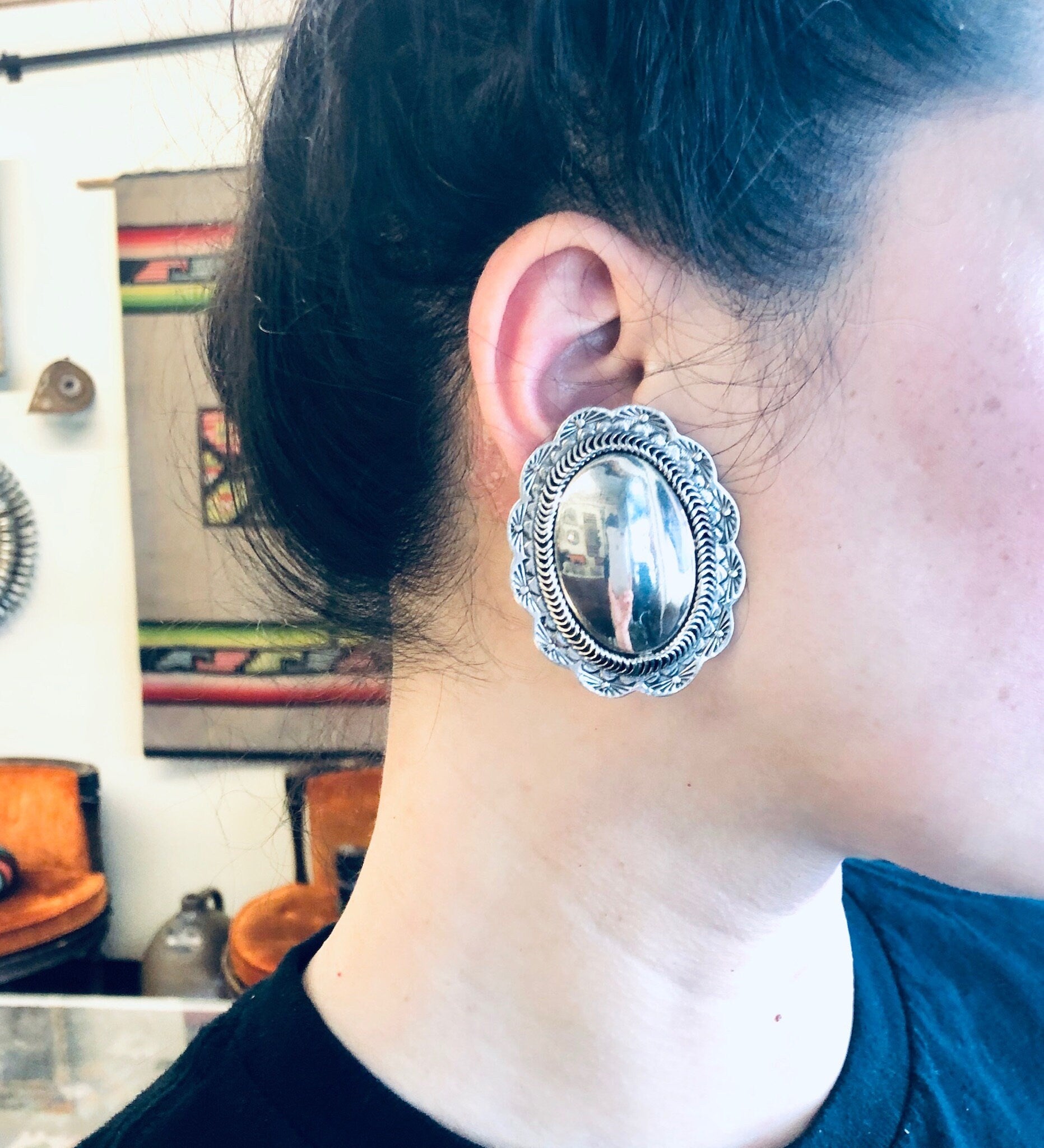 Vintage silver concho clip-on earrings worn by a person with dark hair, showcasing the large, unique statement jewelry piece against their neck and ear.