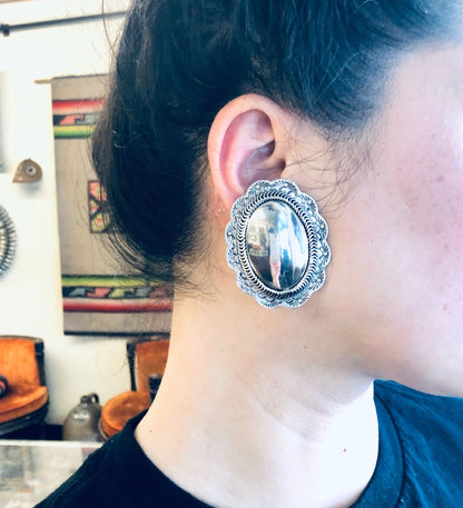 Vintage silver concho clip-on earrings worn by a person with dark hair, showcasing the large, unique statement jewelry piece against their neck and ear.