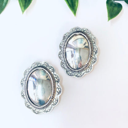 Vintage silver concho clip-on earrings with oval clear stones, shown on white background with green leaves at top.