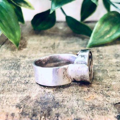 Vintage silver ring with swirl design on textured stone surface, surrounded by green foliage