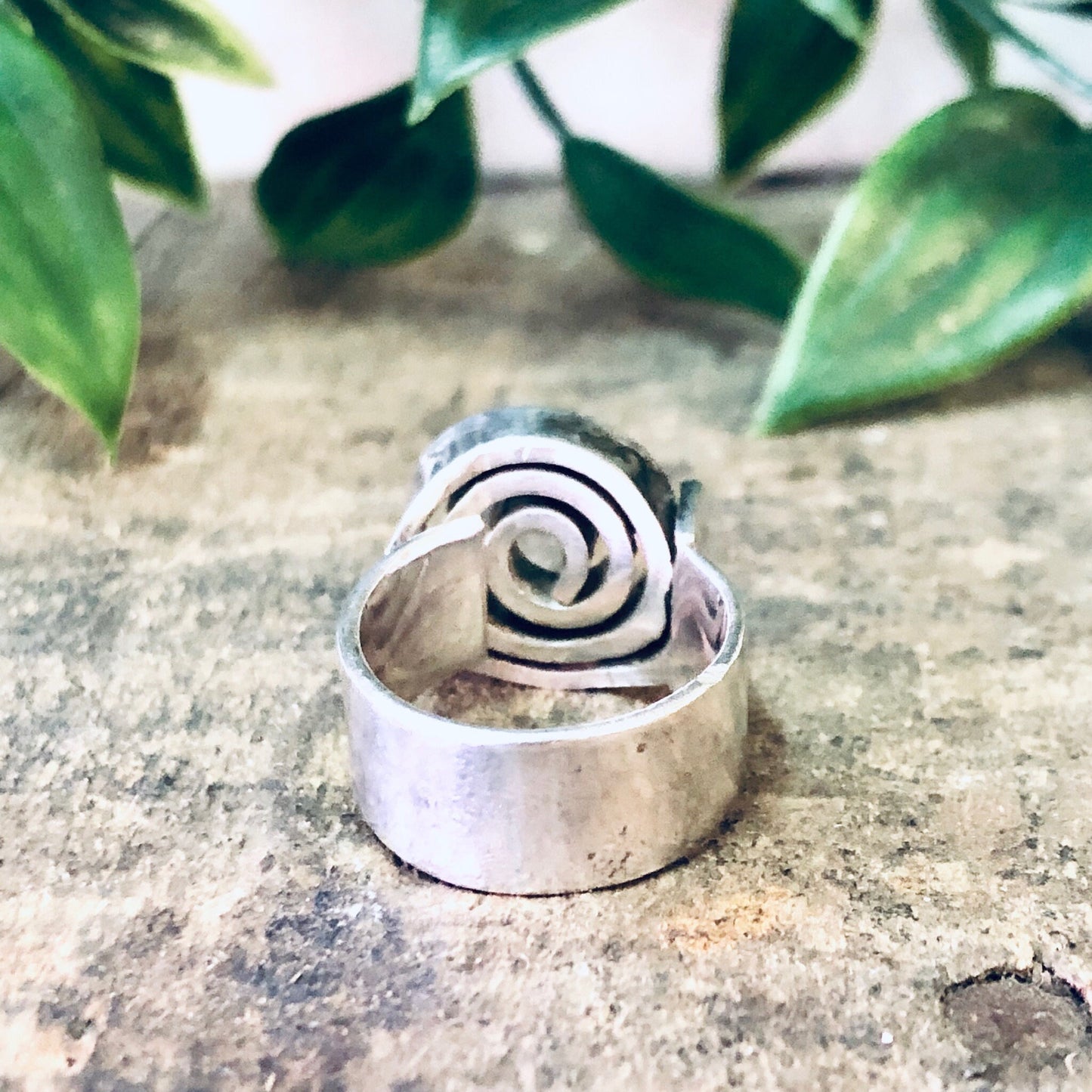 Vintage silver swirl design statement ring on stone surface with green foliage in background, bohemian style modernist thick band jewelry.