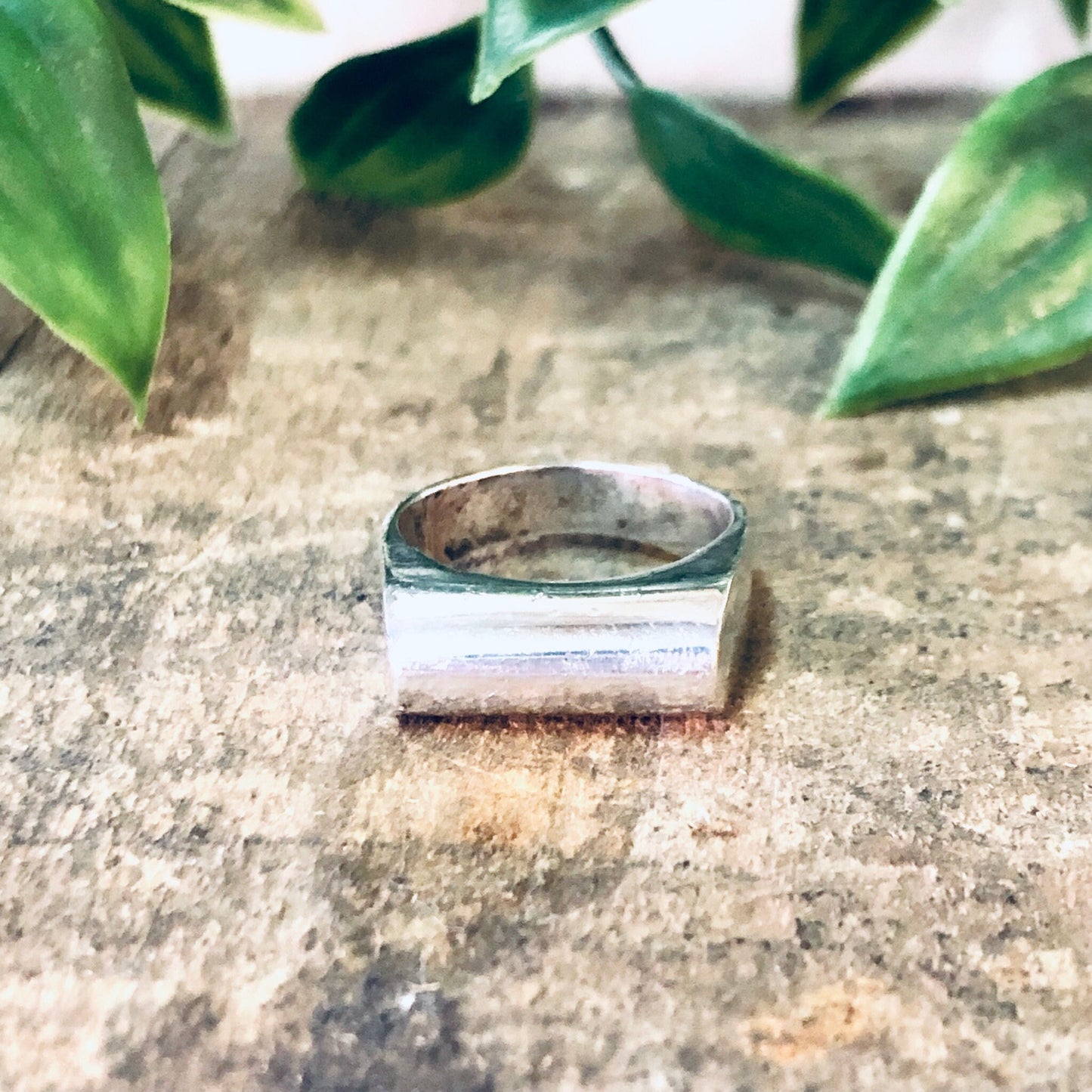 Vintage silver band ring placed on rustic stone surface with green leaves in background, simple modernist jewelry design, unique 925 silver ring.