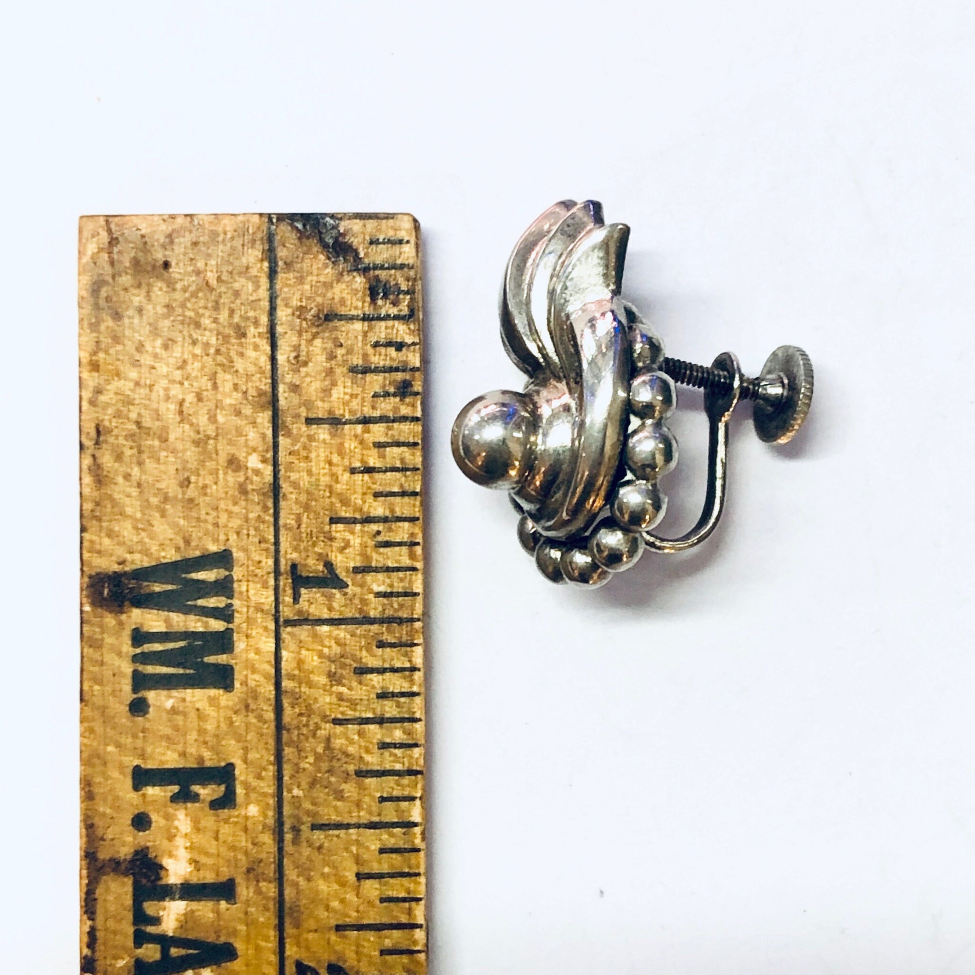 Vintage silver screw back earrings with unique swirl design, placed next to a wooden ruler for scale.