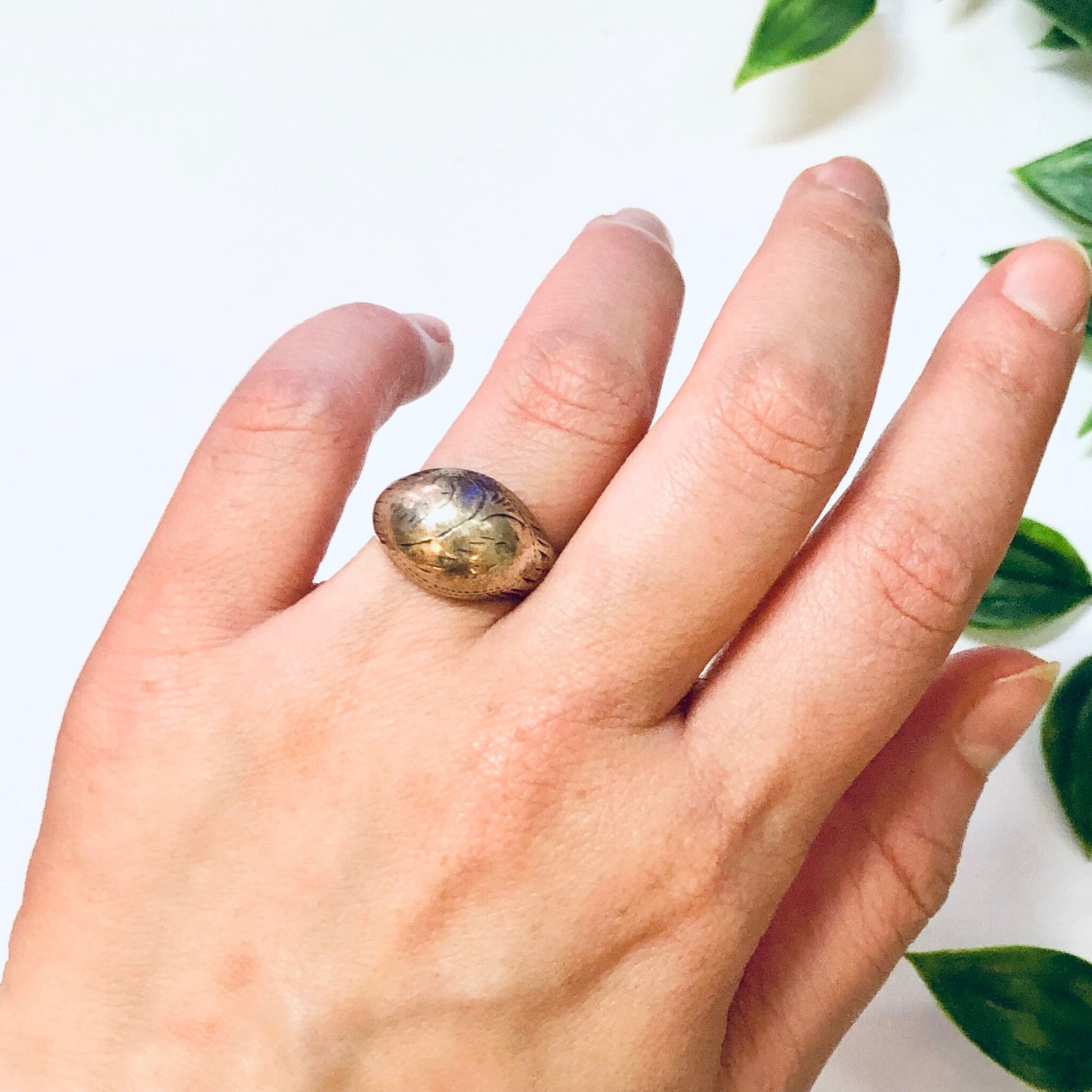 Vintage silver dome ring with an etched floral design held in a hand against a white background with green leaves.