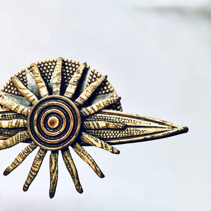 Vintage brass sun-shaped brooch with textured rays and central circle design, resembling a celestial body or planet from the solar system, suitable as unique costume jewelry gift.