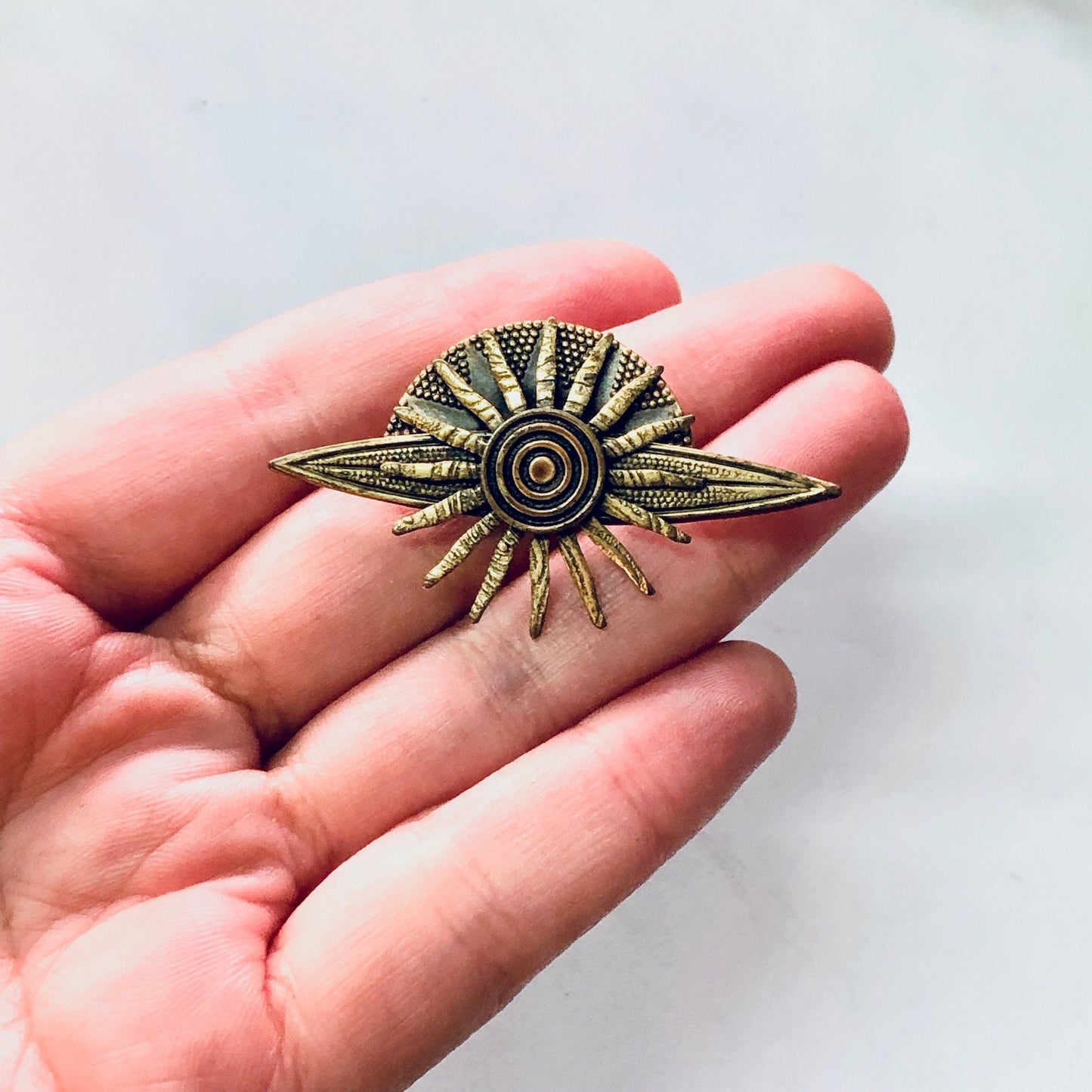 Vintage brass sun brooch held in palm of hand