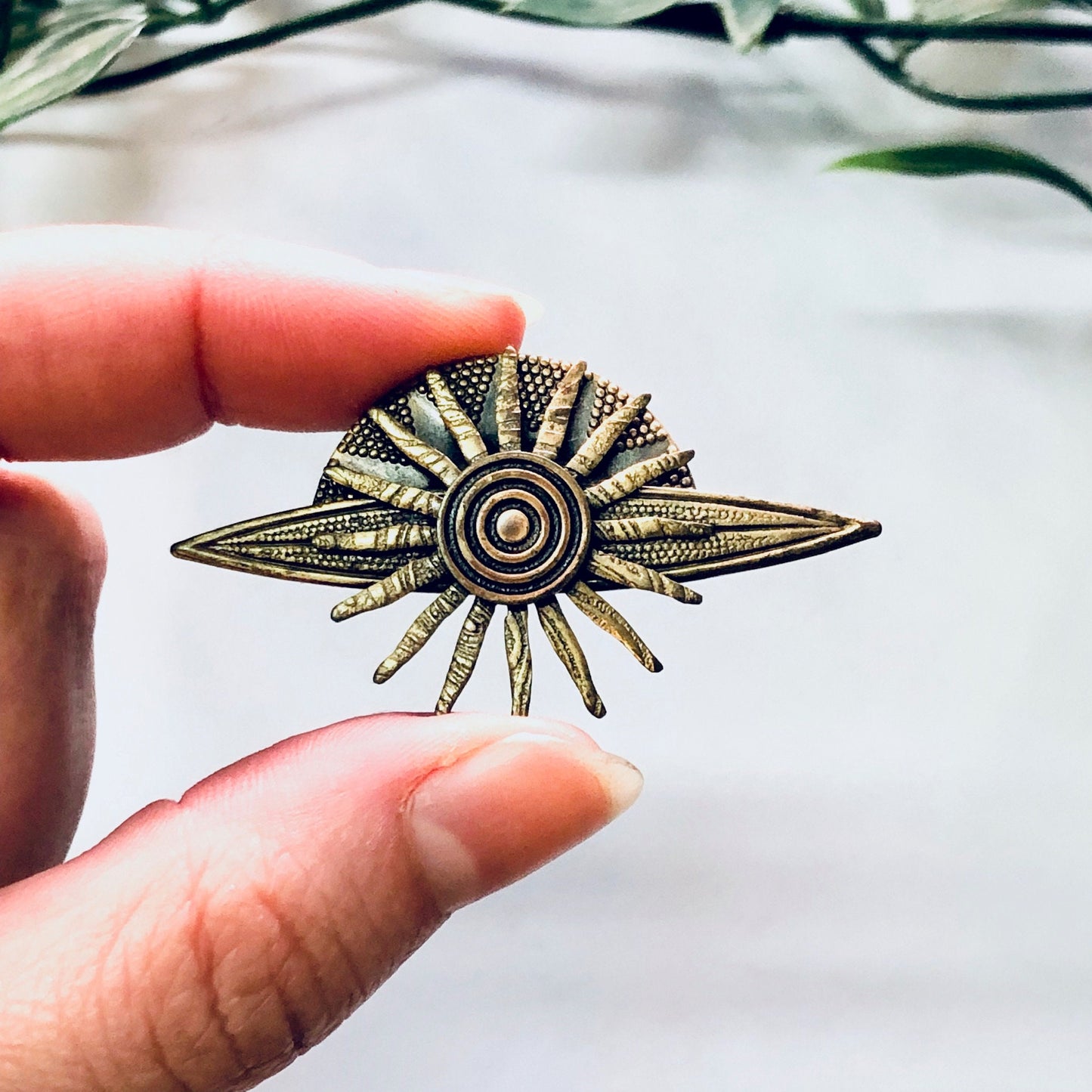 Vintage brass-toned sun brooch or pin held in hand, resembling a planet or solar system, showing intricate design details. Suitable as gift idea or costume jewelry piece from vintage collection.