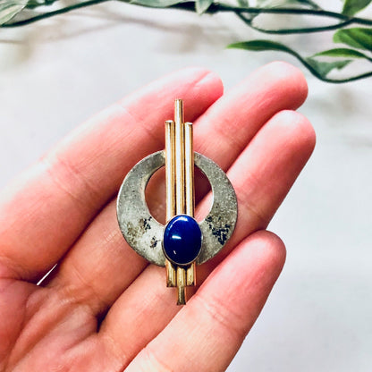 Vintage silver and gold brooch with blue stone in an abstract minimalist design, held in palm of hand