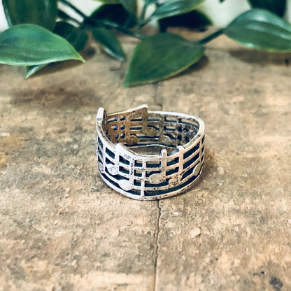 Vintage silver treble clef musical note ring on stone surface with plant leaves in background