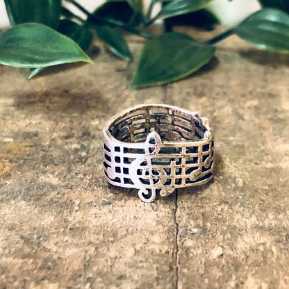 Vintage silver treble clef musical note ring on rustic wooden surface with greenery in background