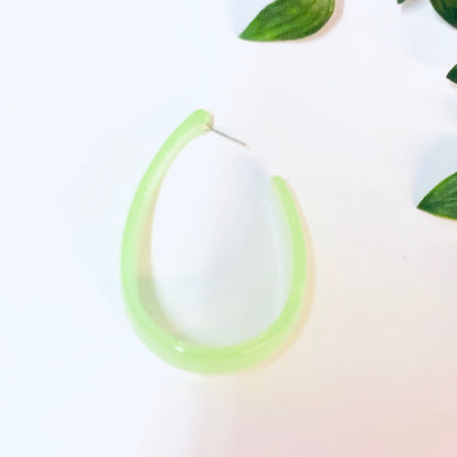 Neon green translucent plastic hoop earrings on white background with leaves