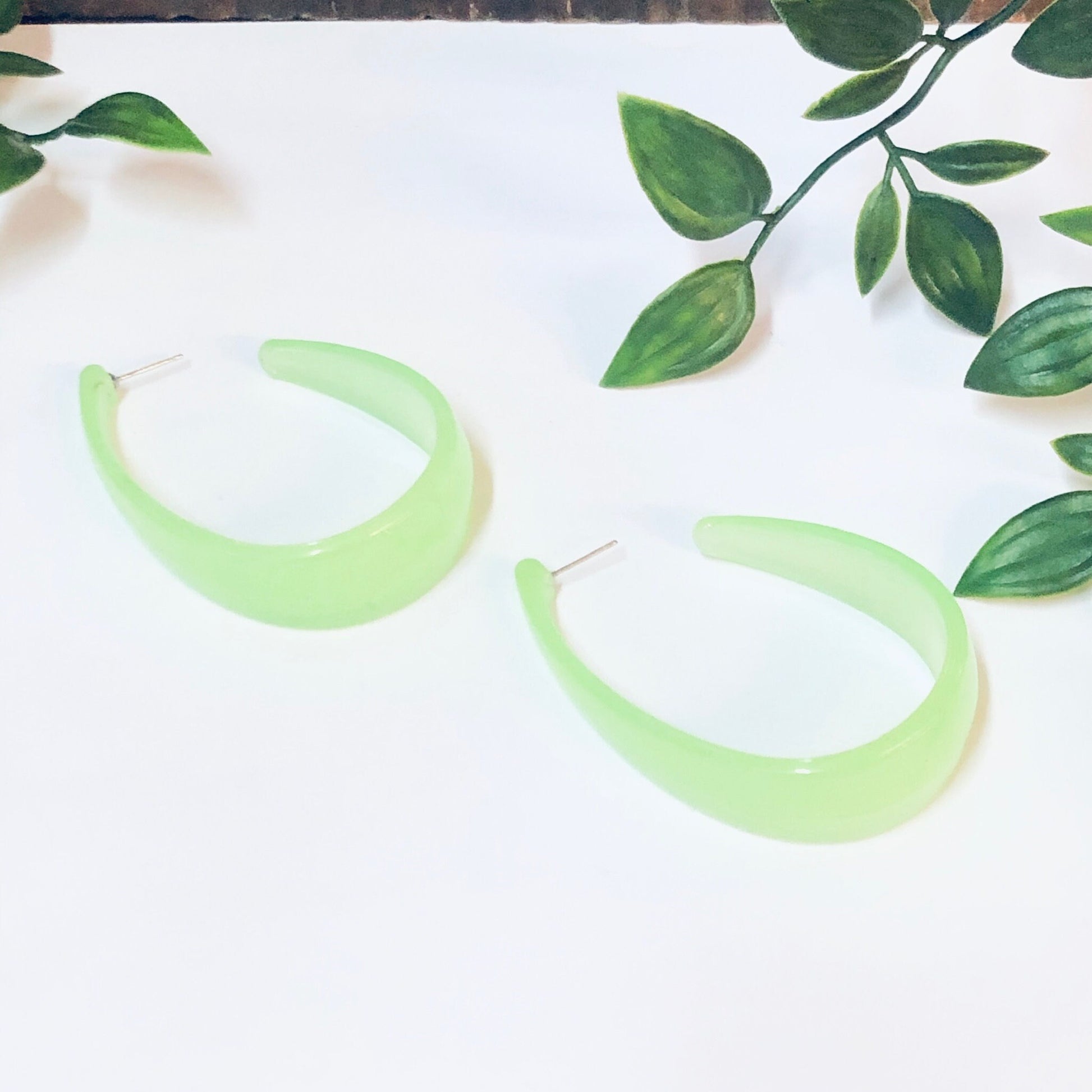 Neon green crescent hoop dangle earrings on white background with leafy green branches