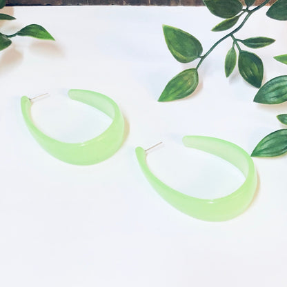 Neon green crescent hoop dangle earrings on white background with leafy green branches