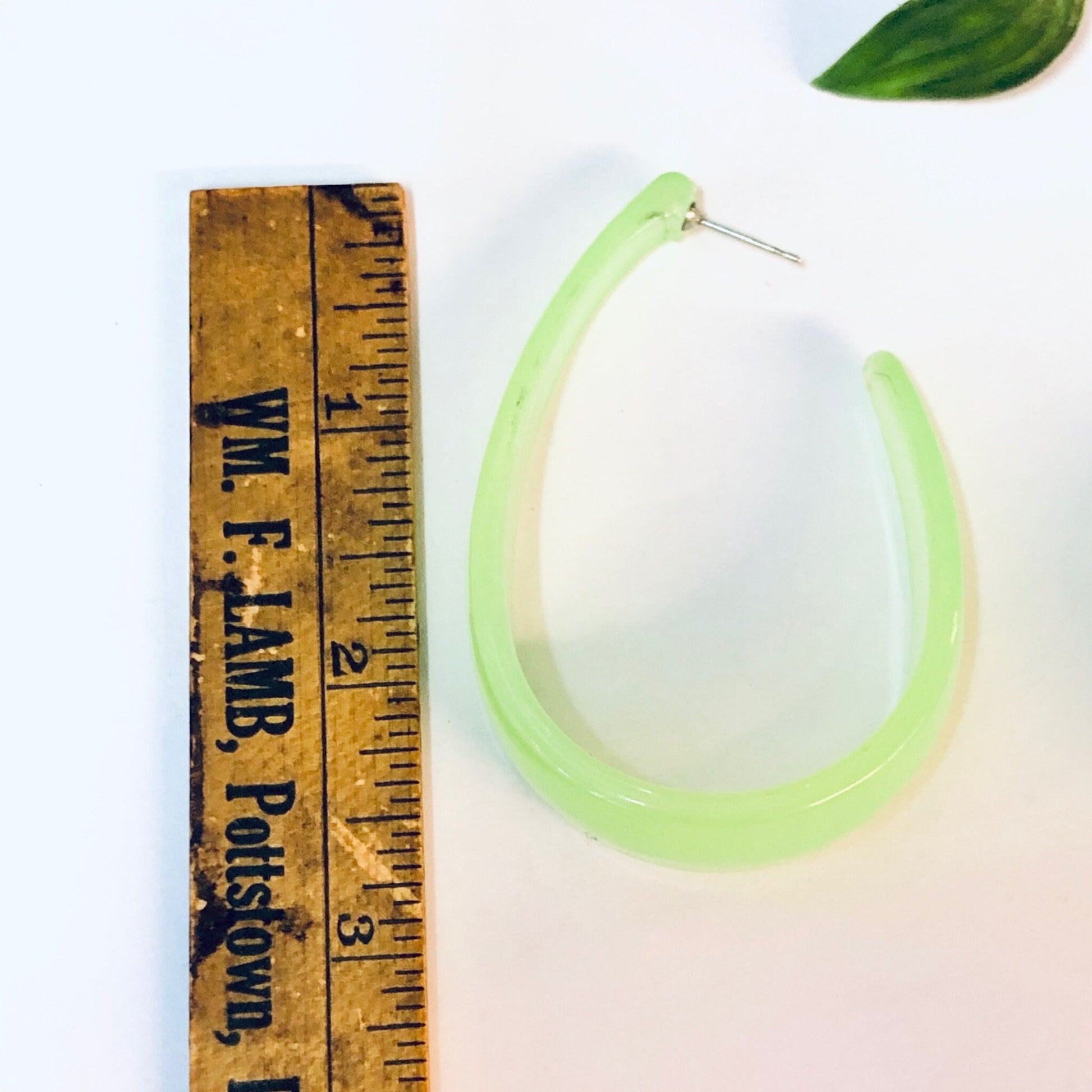 Vintage neon green transparent plastic hoop dangle earrings next to ruler for scale