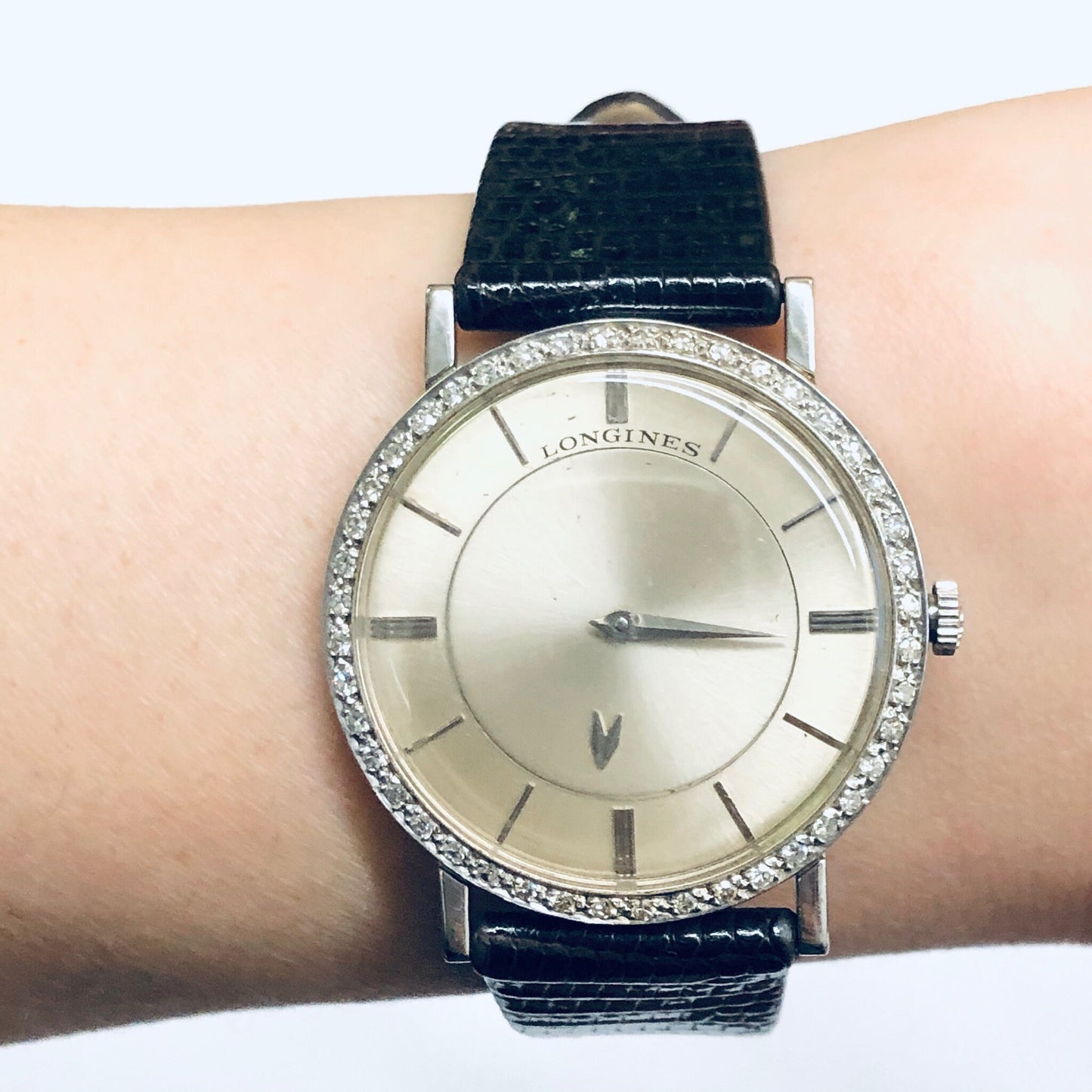 Vintage Longines mystery dial watch with 18K white gold case, diamond bezel, and navy blue leather strap on a person's wrist.