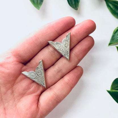 Vintage silver collar tips with swirl design held in palm of hand against white background with green leaves