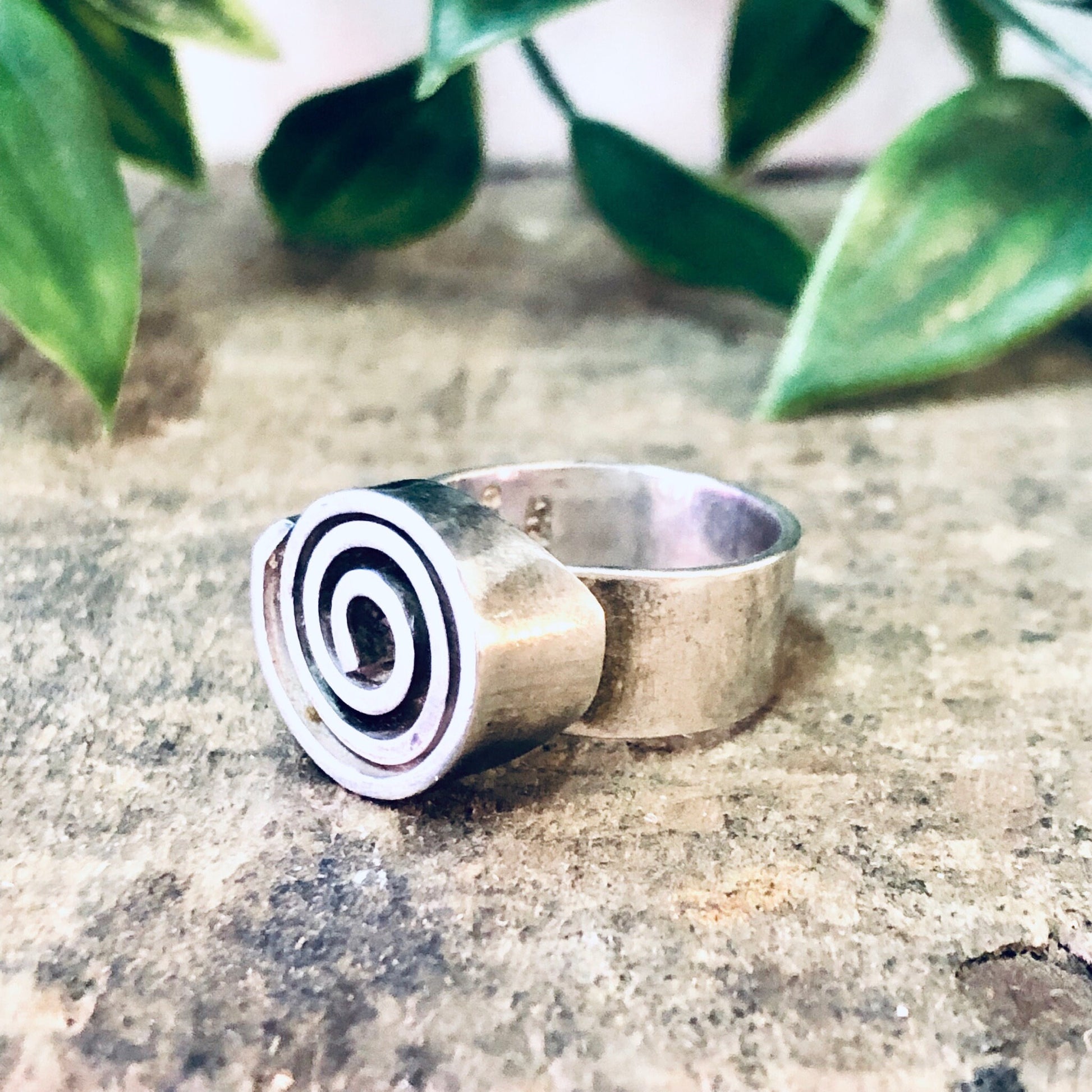 Vintage silver swirl design statement ring on stone surface with green leaves in background, thick band bohemian modernist jewelry.