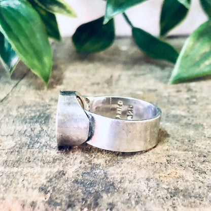 Vintage silver ring with swirl design on textured background with green leaves, bohemian statement jewelry piece.