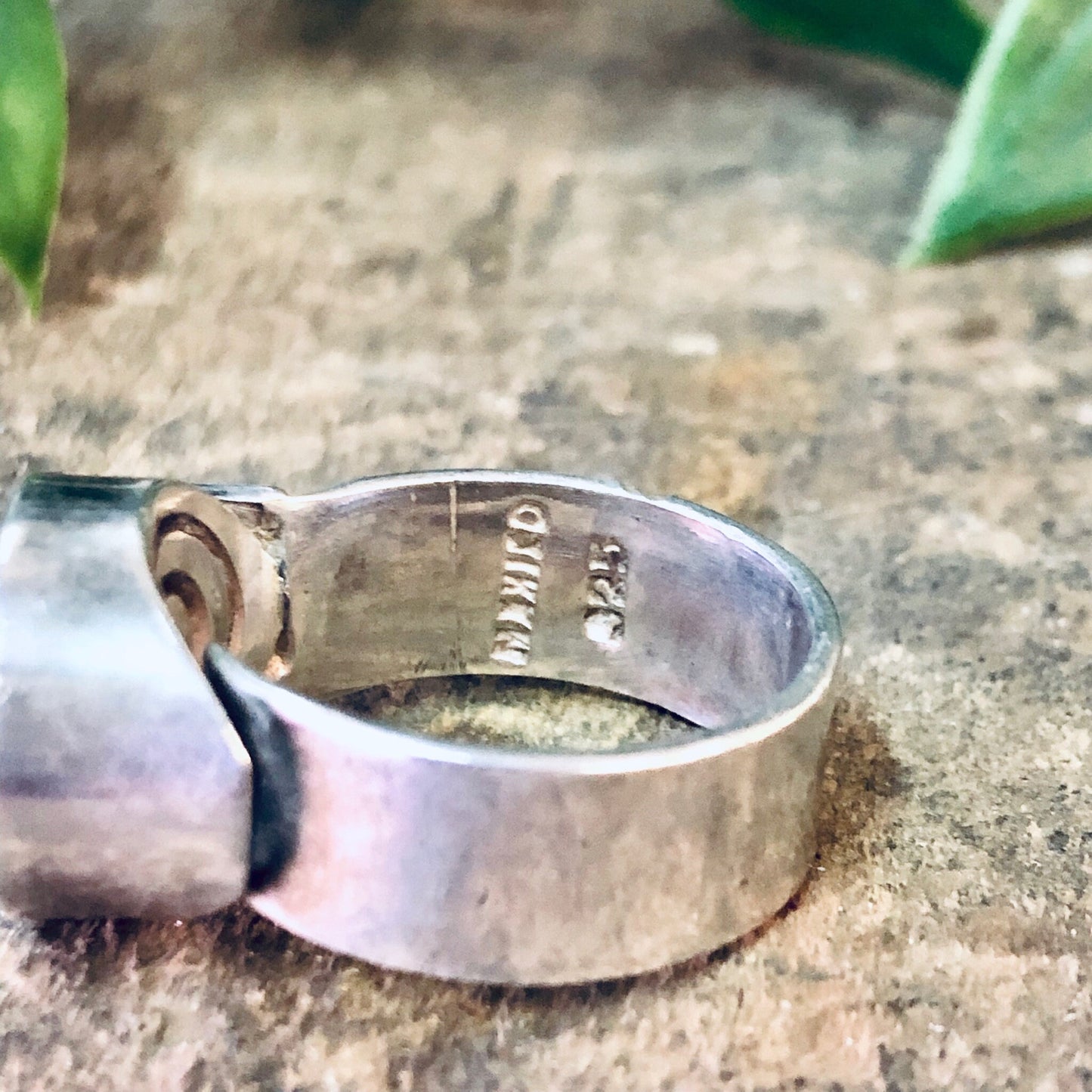 Vintage silver ring with swirl design on a textured surface next to green leaves, bohemian modernist statement jewelry with thick band