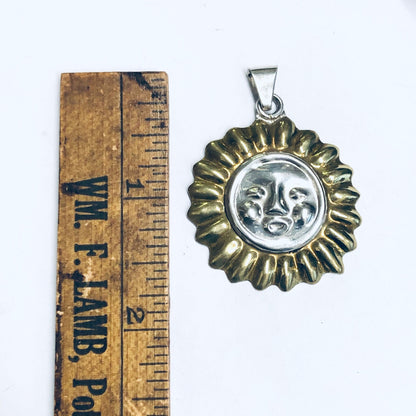 Silver sun face pendant with gold accents on vintage wooden ruler