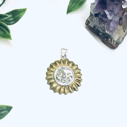 Vintage silver sun face pendant charm with gold accents surrounded by green leaves and amethyst crystal on white background