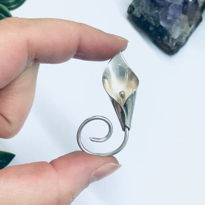 Silver calla lily flower brooch pin held in hand against amethyst crystal, vintage floral jewelry closeup