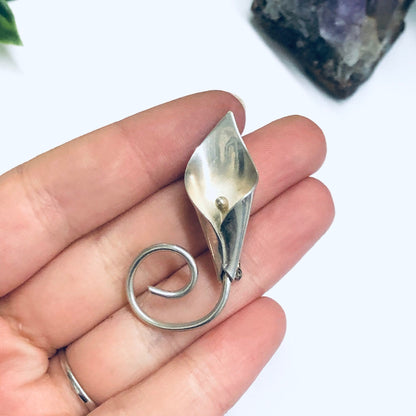 Silver calla lily brooch pin held in hand with amethyst crystal in background