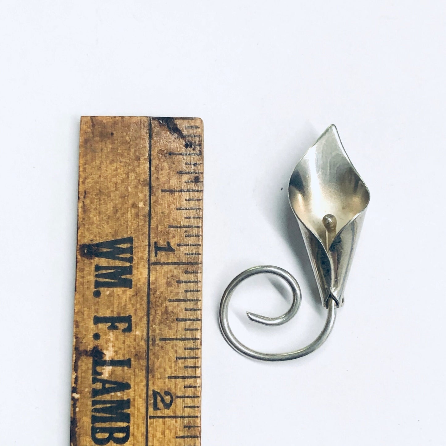 Silver calla lily brooch pin against wooden ruler, vintage floral jewelry