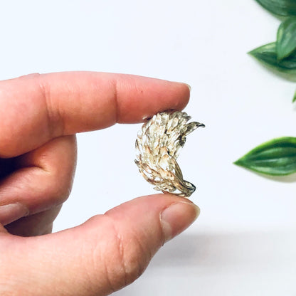 Vintage silver feather or leaf shaped earrings held in fingers against a white background with green leaves.