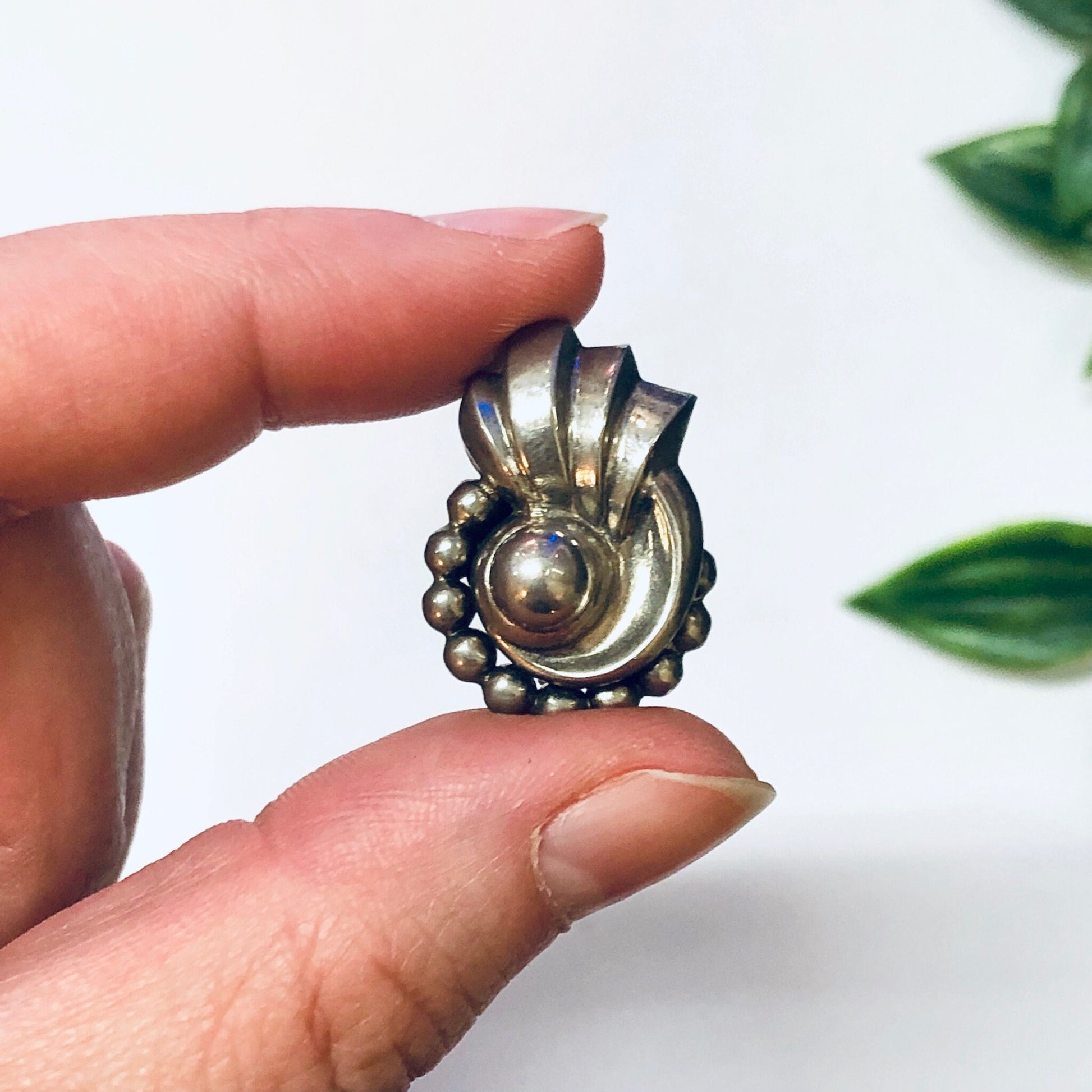 Vintage silver screw back earrings with unique swirl design featuring a round center cabochon, held by hand against a white background with green leaves.