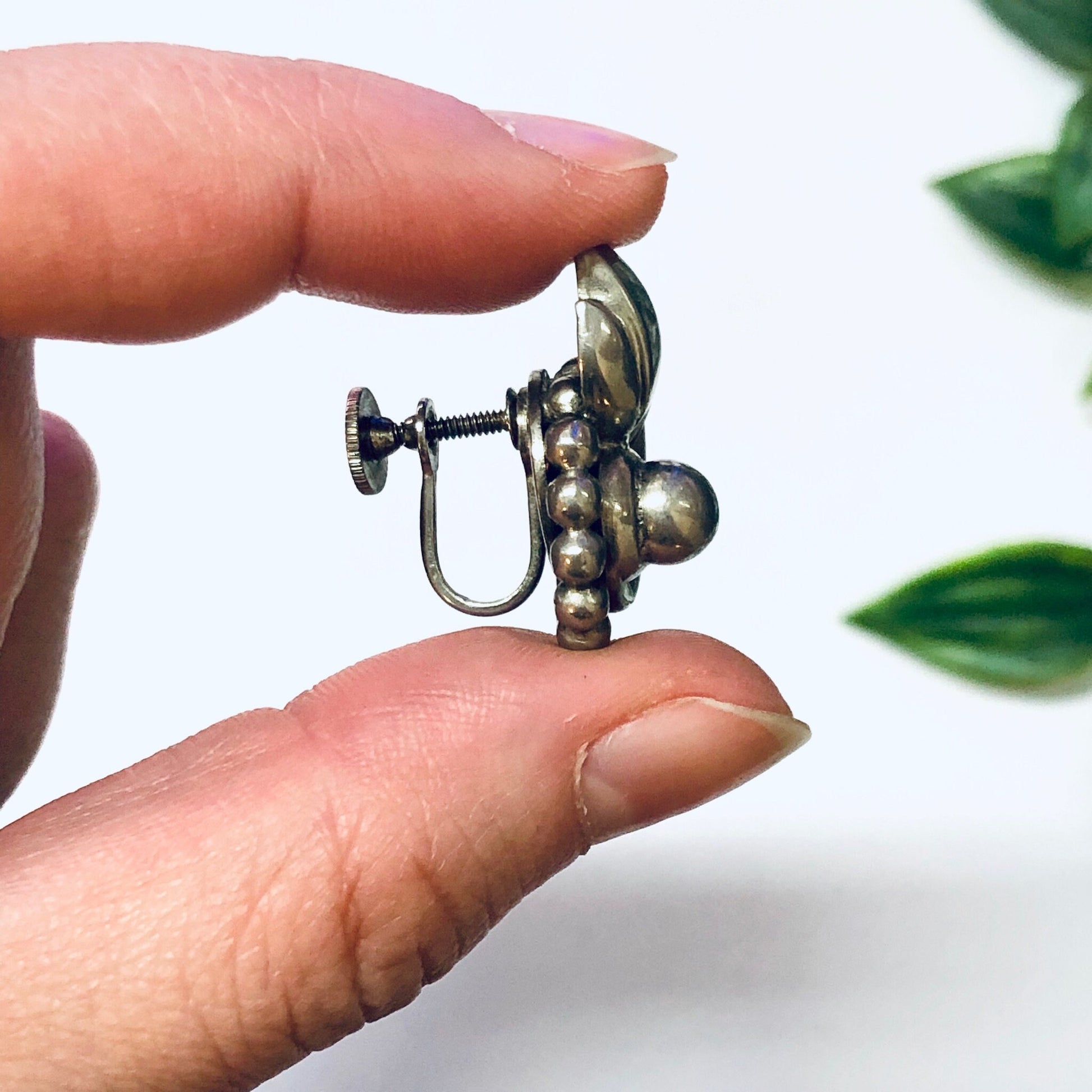 Vintage silver screw back earrings with unique dangly ball design, held in hand against white background with green leaves.