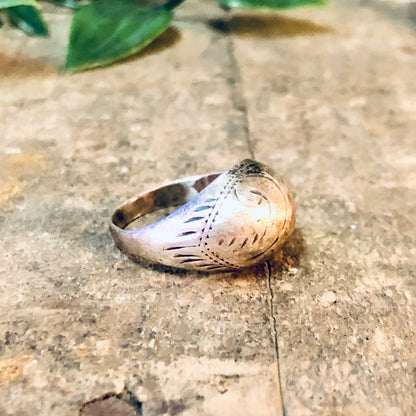 Vintage silver dome ring with etched design on worn concrete surface with green leaves in background