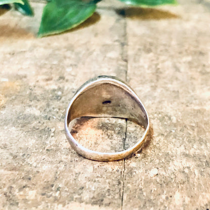 Vintage silver dome ring with etched design on concrete surface next to green leaves