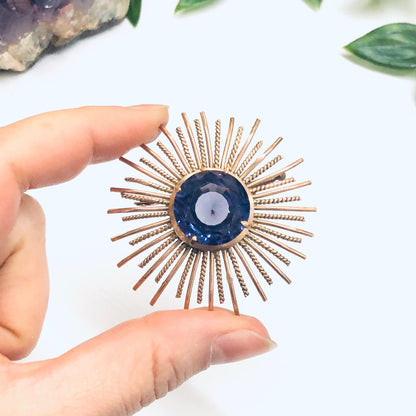 Vintage sunburst brooch with Alexandrite gemstone held in fingers against white background with leaves