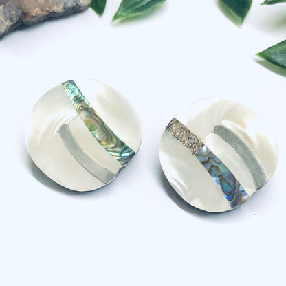 Vintage abalone shell clip-on earrings with abstract mother of pearl inlays, displayed on a white background with green leaves.