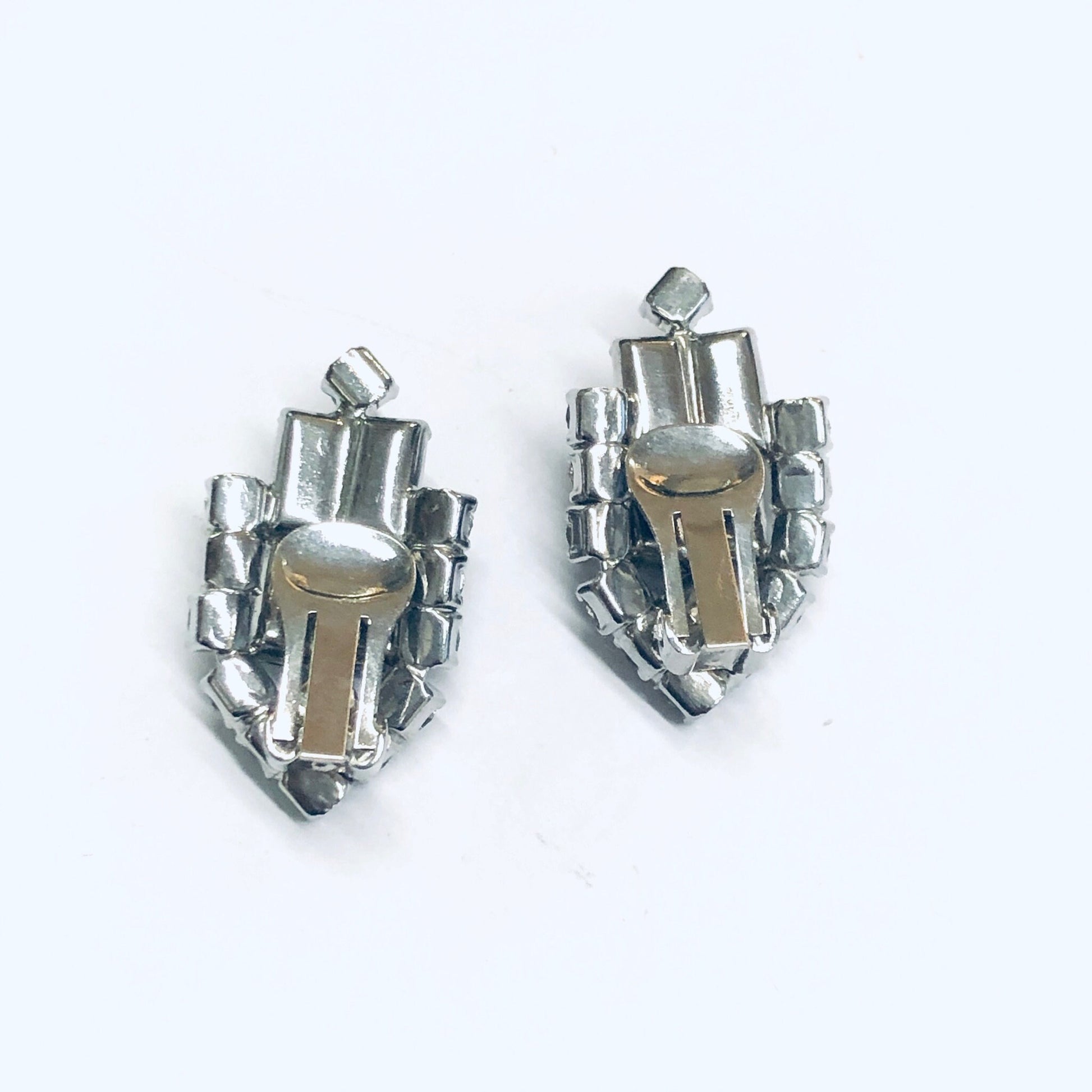 Silver and gold colored rhinestone clip-on earrings in a vintage shield design, photographed on a plain white background.