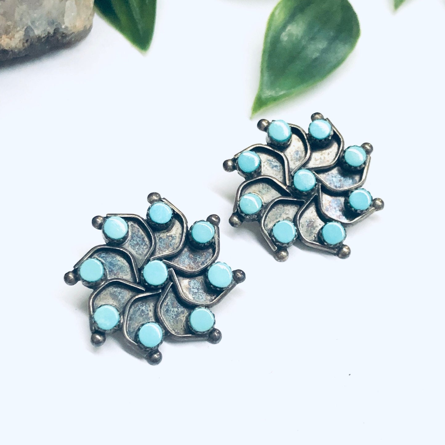 Silver and turquoise star-shaped vintage clip-on earrings on white background with green leaves